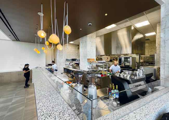 The L-shaped exhibition kitchen contributes to staff efficiency. Buoy-style fixtures help light the space. Photo by Nahum Goldberg