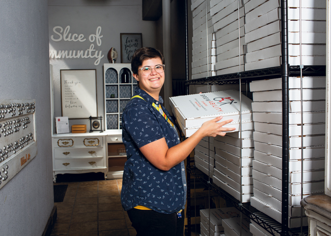 Madison Sherock removes pizza boxes from a shelving unit placed in a hallway outside the kitchen.
