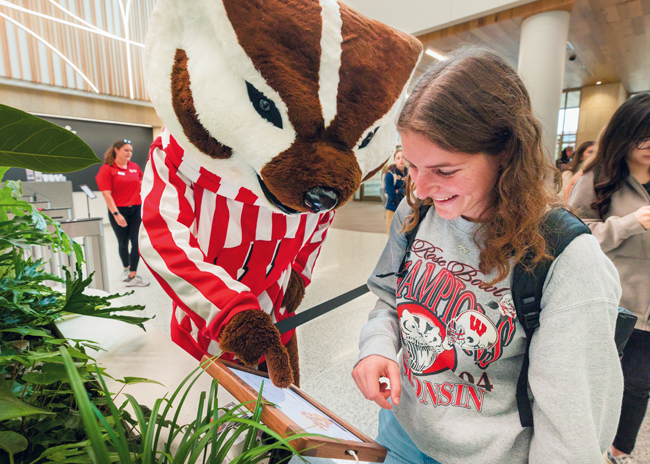 The University of Wisconsin-Madison mascot Bucky Badger walks a student through touch-pad ordering. 