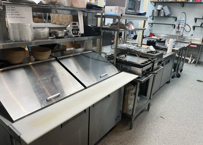 After cooking, cafe orders are assembled using a sandwich table. A pair of tabletop steam wells hold cooked proteins that are warmed up on the flattop.