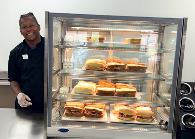 Team member Cameron Scott inspects the display case with deli sandwiches that can be heated in a high-speed oven.