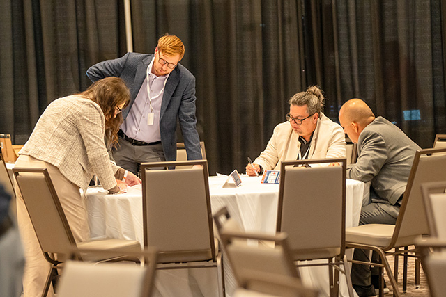 Brendan Evje (standing, left) and Raul Pineiro work with their peers during a small group session at FEED Workshop 2025